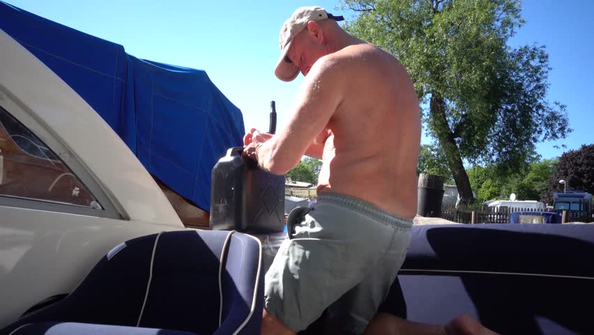 Stockholm, Sweden A man uses a jerrycan to fill a small leisure motorboat with gasoline in a marina on a summer day. 