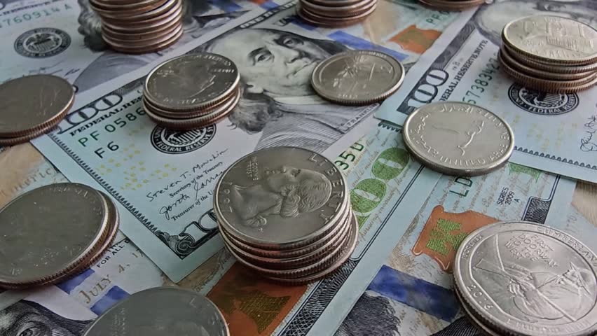 People count stacks of coins and bills on a table. Different types of currency are present. The stacks change as the counting continues in various angles and views.