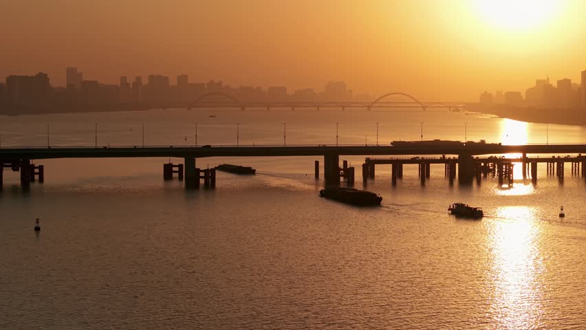 Barges and boats sail on river in Hangzhou, China at golden hour under bridges