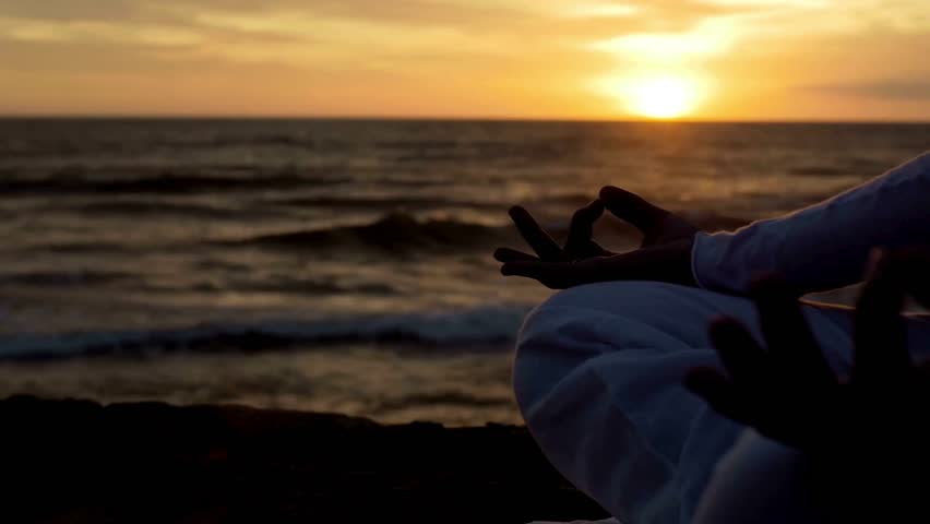 Healthy young woman in front of the sea in lotus pose, meditating at beach on sunset. Concept of healthy life, relaxing, meditating and yoga exercise.