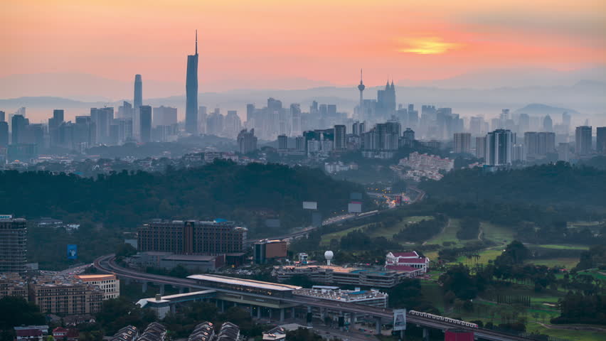 Beautiful dawn time-lapse over the Kuala Lumpur city skyline, featuring iconic skyscrapers under a soft pastel purple and pink morning sky before sunrise. High-angle urban landscape establishing shot. Malaysia. Tilt Up motion timelapse.
