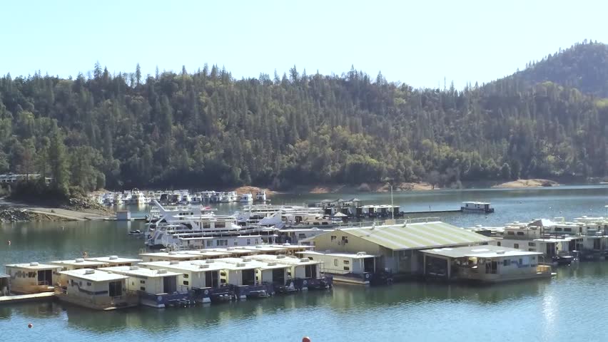 Peaceful Marina Filled with Houseboats Along a Forested Mountain Lake Under Clear Blue Skies.