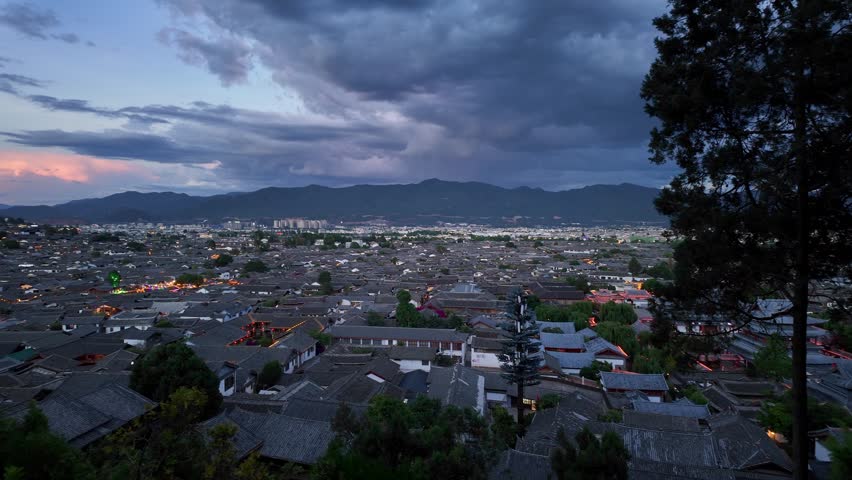 Lijiang, China : Panoramic aerial footage of the Shizi Mountain park overlooking Lijiang old town with the Yulong snow mountain in Yunnan province in China under dramatic sky at sunset