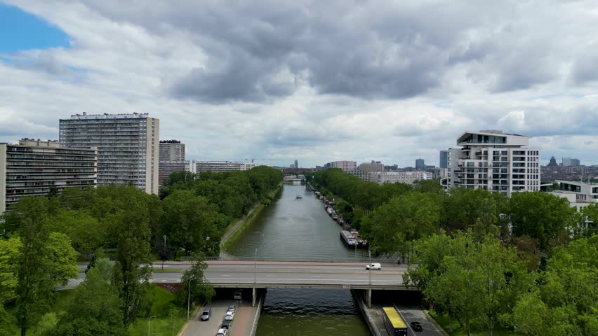 Aerial view of the Brussels-Charleroi Canal with a bridge, apartment blocks, and lush green trees under a cloudy sky in Anderlecht, Brussels, Belgium.