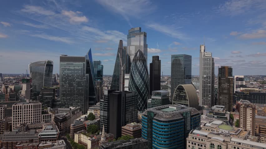 Aerial view of the City of London skyline featuring The Gherkin and modern skyscrapers under a blue sky in London, England, United Kingdom.