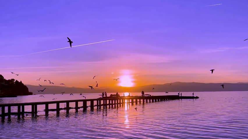 Beautiful Purple Sunset over Sea Pier with Flying Birds and Silhouettes of People.
