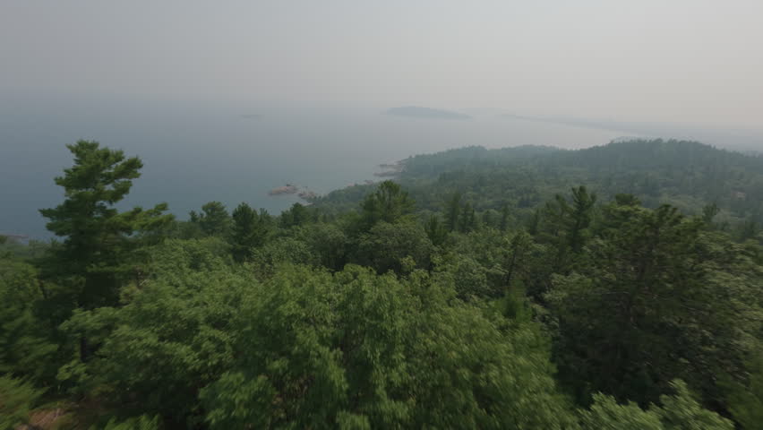 Aerial shot above a lush forest on Sugarloaf Mountain revealing a hazy lake superior shoreline