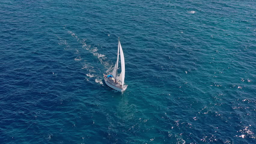 Drone footage of sailboats with bright white sails gliding together through calm Mediterranean waters on a sunny sailing holiday