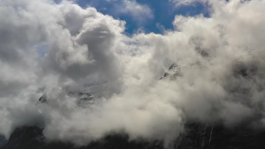 Clouds drift across snow-capped peaks with mesmerizing motion.