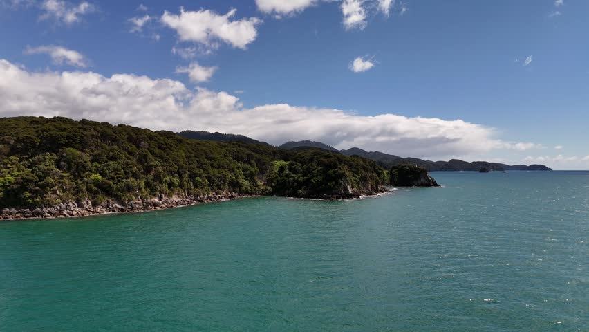 Rising drone shot revealing a dense native forest headland surrounded by vibrant turquoise waters in Abel Tasman.