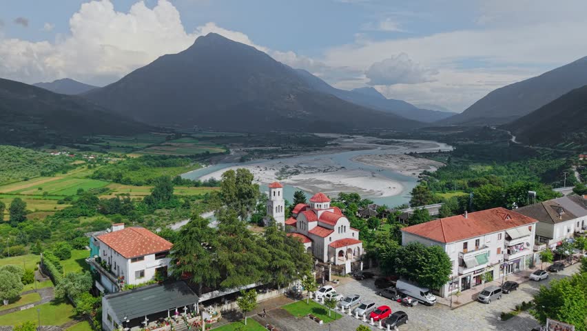 Aerial view of an Orthodox church with red roofs overlooking the Vjosa River valley and surrounding mountains in Tepelene, Gjirokaster County, Albania.