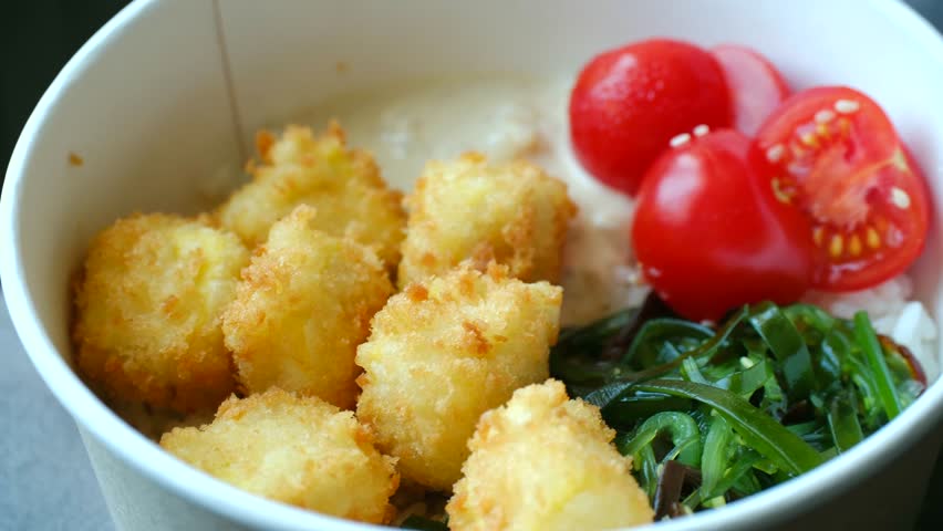 Takeaway poke bowl with fried tofu cherry tomatoes, wakame seaweed salad over bed of rice with creamy sauce. Asian food for healthy and balanced meal. Healthy poke bowl with fried tofu cherry tomatoes