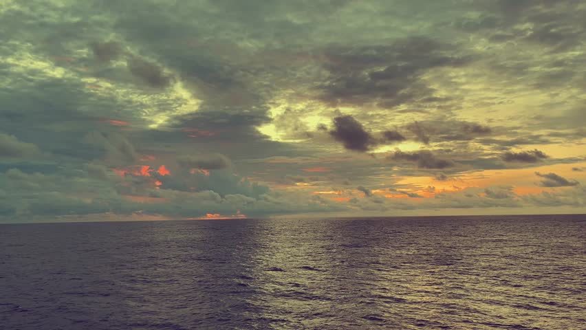 Sunrise over the ocean with clouds reflecting warm light on the water surface