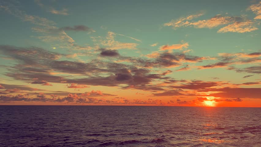 Sunset over a calm ocean with vibrant clouds creating a serene and picturesque seascape