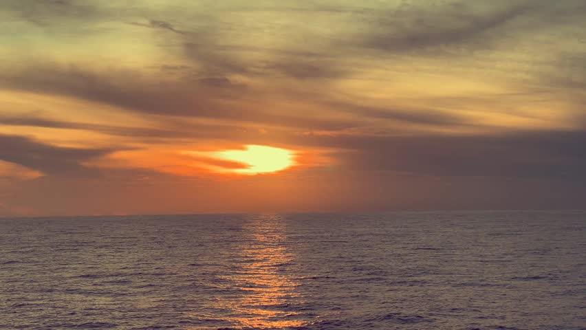 Sunset Over a Calm Ocean with Soft Clouds in the Sky and Gentle Waves on the Water
