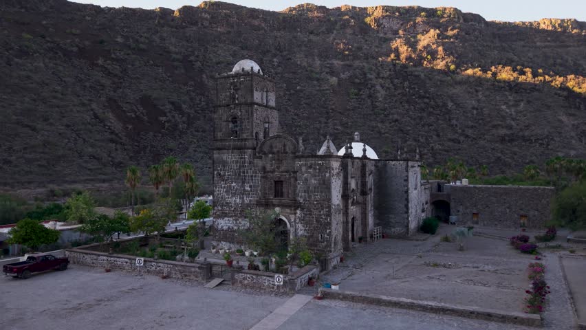 View aerial shots of San Javier Mission as the sun rises over the oasis and palm trees in Baja California Sur, near Loreto