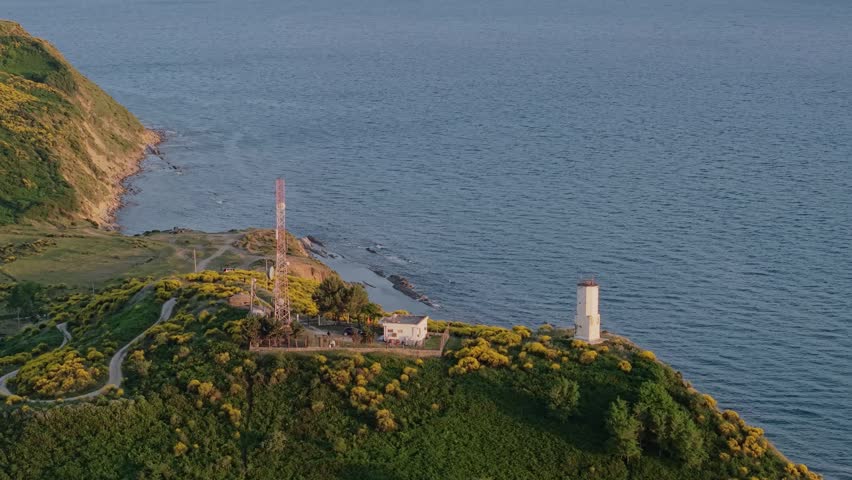 Aerial view of a lighthouse and communication tower on a green hill with yellow flowers in the Vjose-Narte Delta Protected Area, Zvernec, Vlore County, Albania.