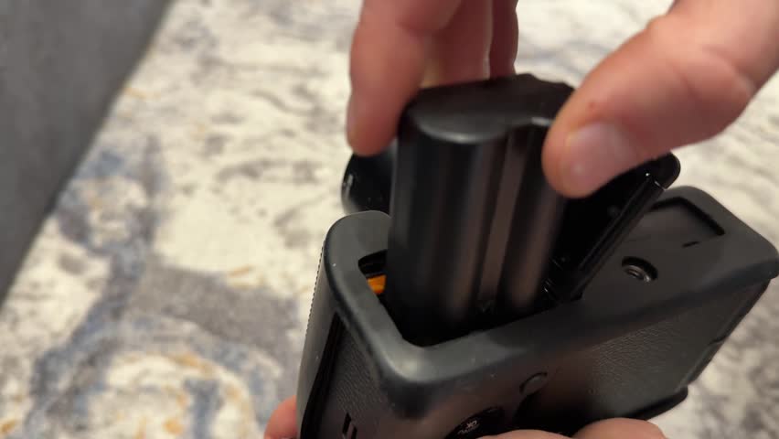Hands inserting battery into camera charger dock, charging photography equipment power pack concept.