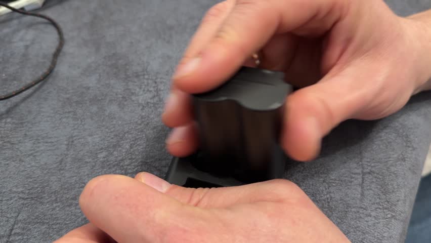 Hand placing camera battery on charger dock, recharging digital camera power pack and photography equipment concept.