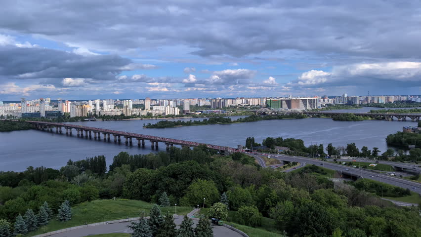 Wide panoramic view of Kyiv left bank residential districts and Paton bridge across the Dnieper river with highway traffic under a cloudy sky