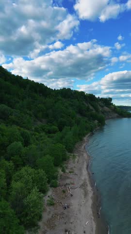 Cinematic aerial footage of the Scarborough Bluffs during golden hour in Toronto, Ontario, Canada. Drone view captures the iconic white cliffs, sandy shoreline, gentle waves of Lake Ontario, and warm sunset light illuminating the natural coastal landscape.