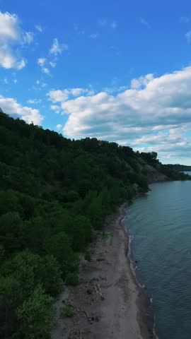 Cinematic aerial footage of the Scarborough Bluffs during golden hour in Toronto, Ontario, Canada. Drone view captures the iconic white cliffs, sandy shoreline, gentle waves of Lake Ontario, and warm sunset light illuminating the natural coastal landscape.