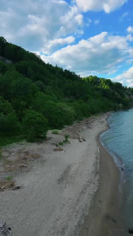 Cinematic aerial footage of the Scarborough Bluffs during golden hour in Toronto, Ontario, Canada. Drone view captures the iconic white cliffs, sandy shoreline, gentle waves of Lake Ontario, and warm sunset light illuminating the natural coastal landscape.