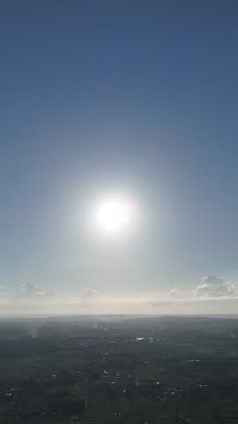 Vertical aerial view of the bright sun shining in a clear blue sky over a distant hazy land horizon