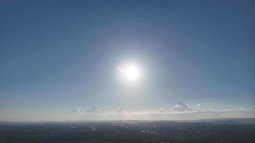 Wide aerial view of the bright sun shining in a clear blue sky over a distant hazy land horizon
