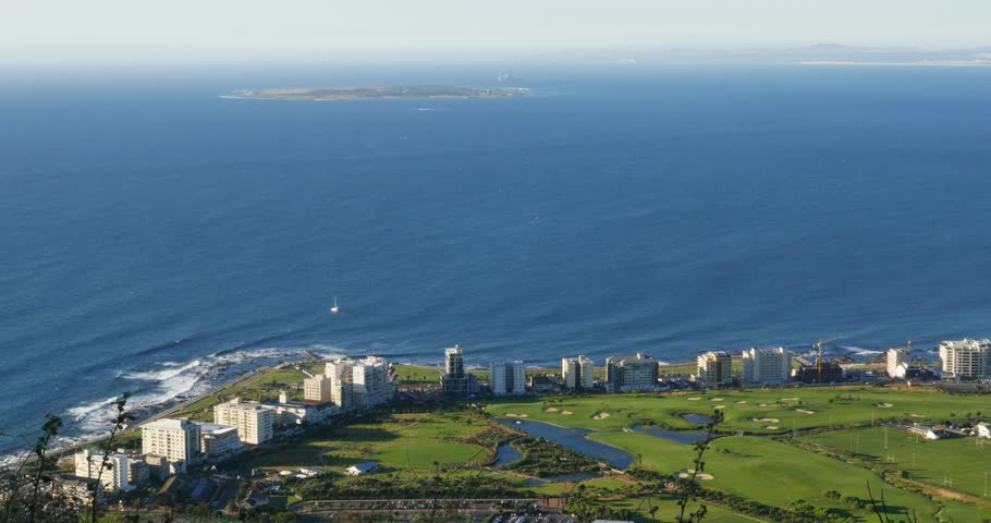 4K footage from Signal Hill of Green Point’s hotels and luxury apartments, Robben Island visible offshore in Table Bay. A scenic Cape Town city and coastal landscape in Western Cape, South Africa.