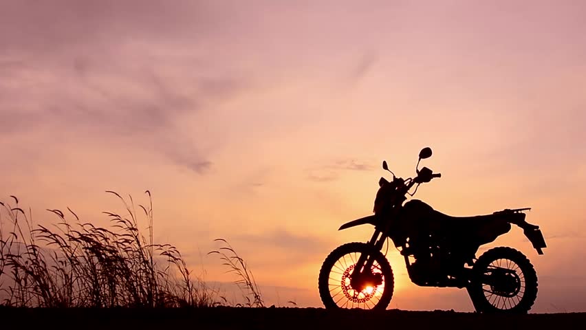 Silhouette of a dirt bike at sunset with dry grass in the foreground