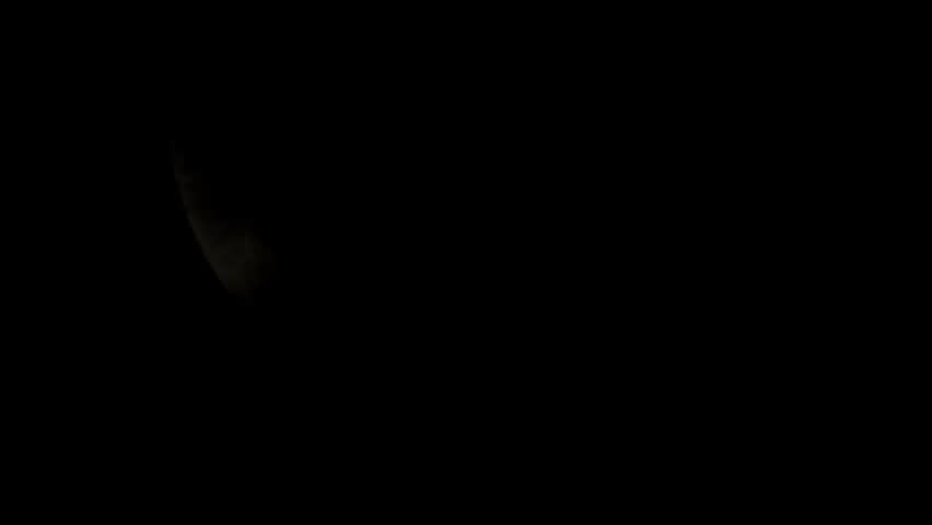 A close-up view of the moon with its craters visible, set against a dark, starry sky. The moon is partially illuminated, casting dramatic shadows across its surface