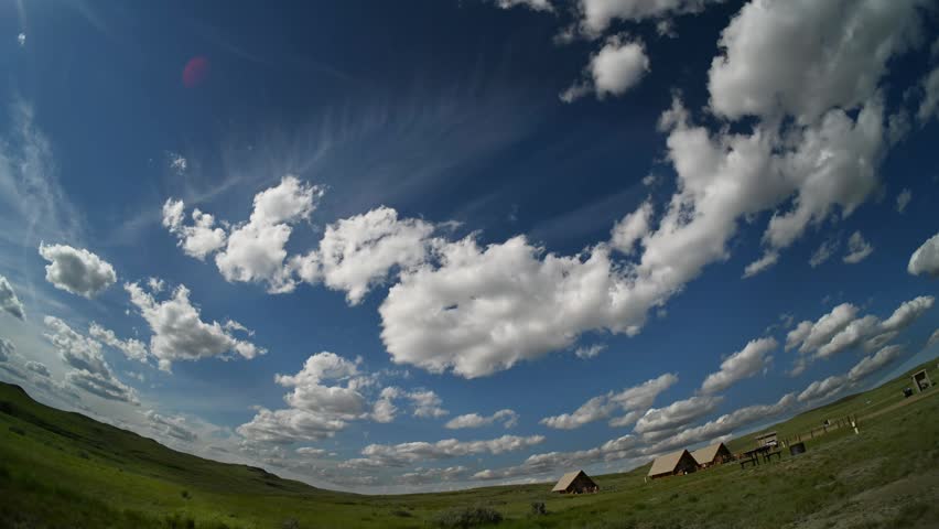 Fish-eye timelapse of white summer cumulus clouds drifting above a prairie park with camping tents