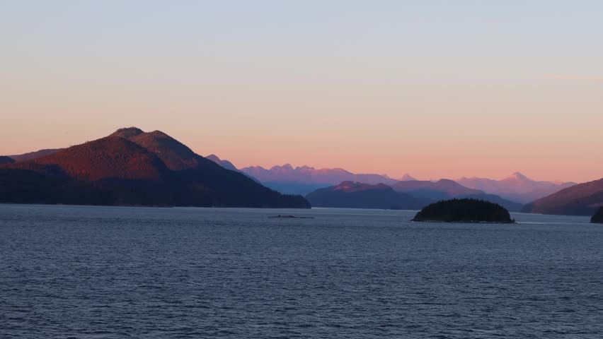 Aerial view of the Inside Passage featuring forested islands and distant mountain peaks under a soft pink sunset sky in Ketchikan Gateway Borough, Alaska, United States.