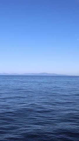 Aerial view of the deep blue sea with gentle ripples under a clear sky and a distant mountain range on the horizon in Juneau, Alaska, United States.