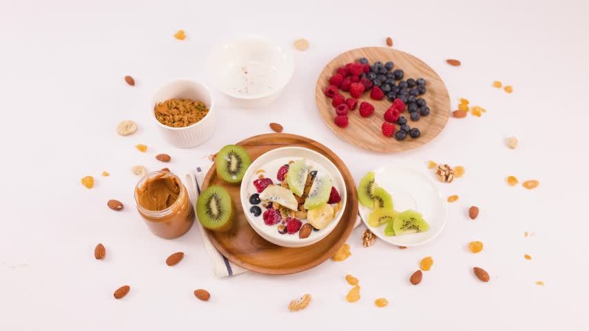 Overhead view of hands lifting a yogurt bowl filled with berries, kiwi, and nuts.