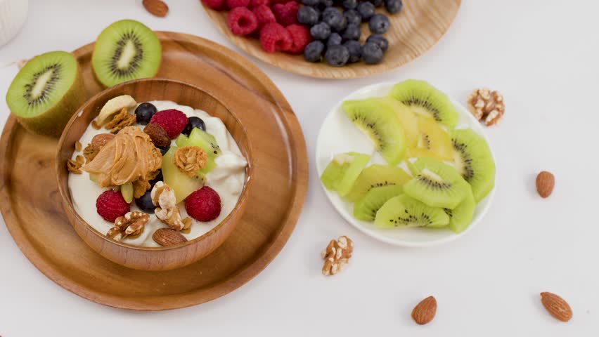 Overhead view of a hand lifting a wooden bowl filled with yogurt, fruit, and granola.
