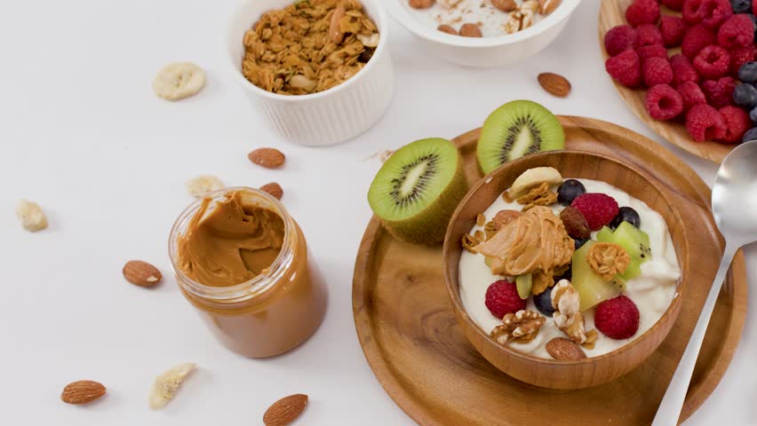 Overhead view of hands scooping yogurt from a bowl filled with fruit and nuts.