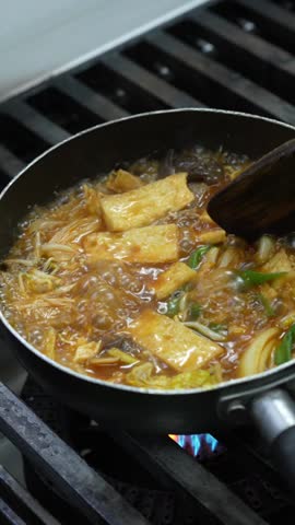 Boiling fish cake soup with noodles and vegetables cooking over a gas stove.
