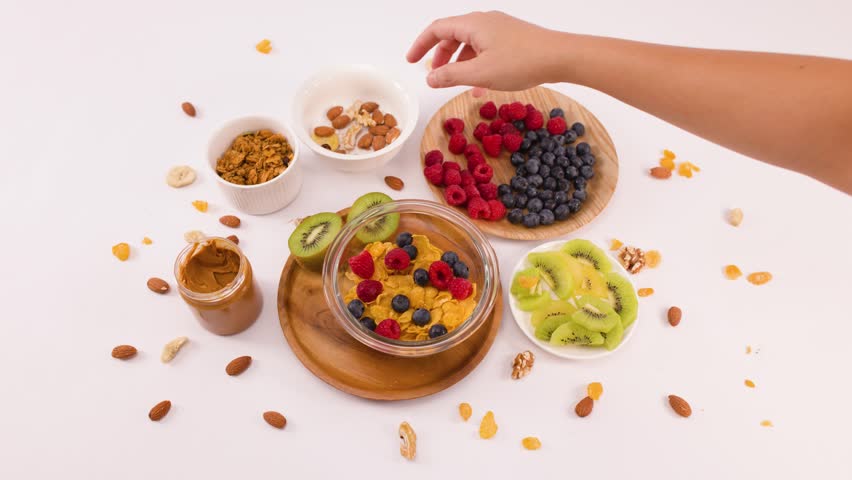 Overhead shot of hand sprinkling walnuts into cereal bowl with berries and kiwi fruit.