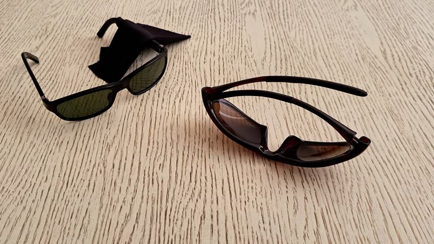 Two pairs of sunglasses placed on a light wooden tabletop. Stylish eyewear with tinted lenses displayed indoors, highlighting fashion accessories, everyday use, and modern style