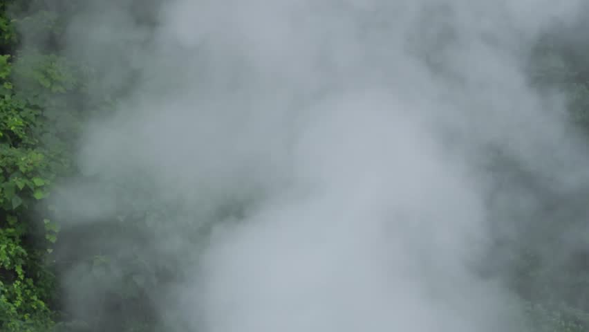 Thick white steam rising and blowing from a natural hot spring pool.