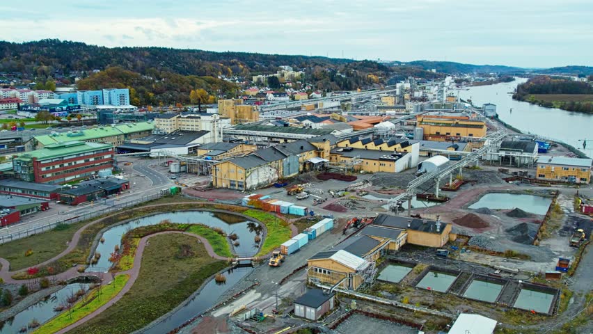 Aerial drone view of industrial area beside river featuring water treatment facility warehouses roads and landscaped retention ponds within urban environment