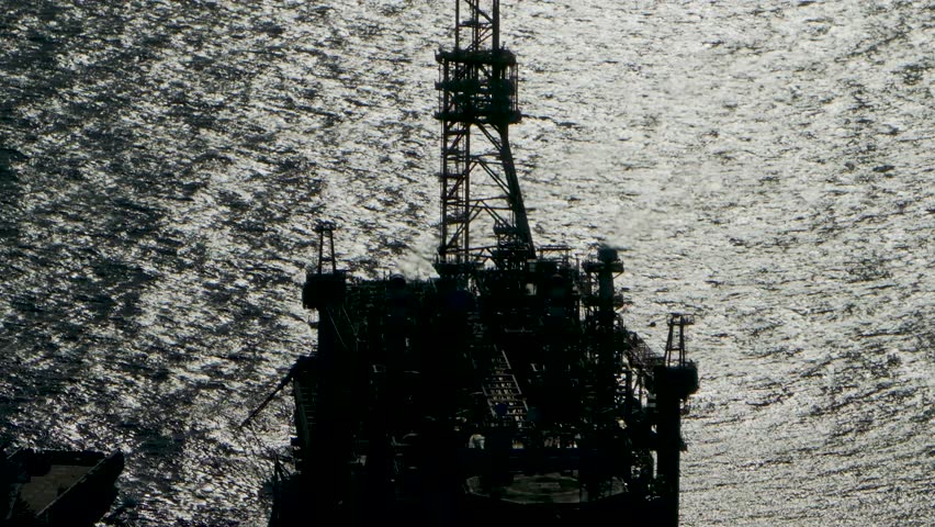 Cinematic close-up aerial footage focusing on the burning gas flare stack of an industrial offshore oil platform set against the backdrop of open deep sea waters.