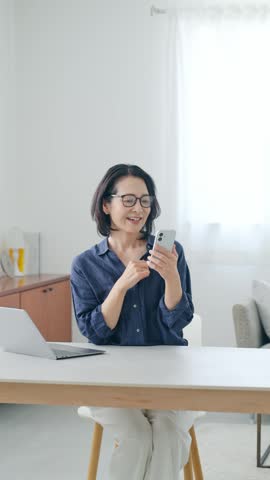 A middle-aged woman looking at her smartphone with joy.