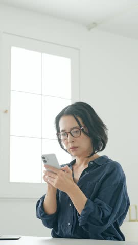 A middle-aged woman looking at her smartphone and worrying.