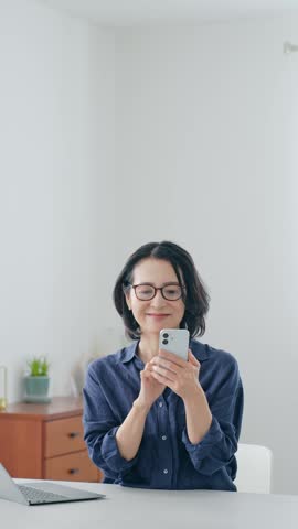 A middle-aged woman smiling while looking at her smartphone.