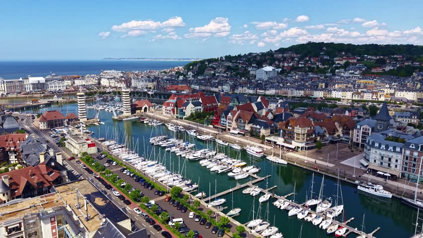 Drone pullback over Deauville marina, sailboats moored, Trouville and sea in background.
