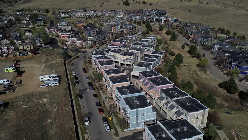Curved boulevard housing bordering Laramie Blvd beside Uptown Broadway, Dakota Ridge rising west in North Boulder. Flat roofs, aligned façades, pale tones, crisp shrub shadows on pavement in CO. USA