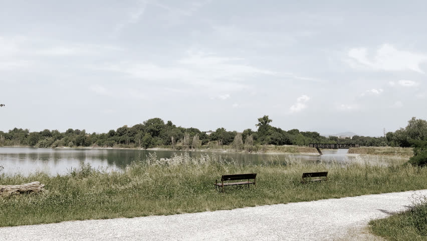 Beautiful landscape view of a calm lake with empty park benches and a walking path on a bright day